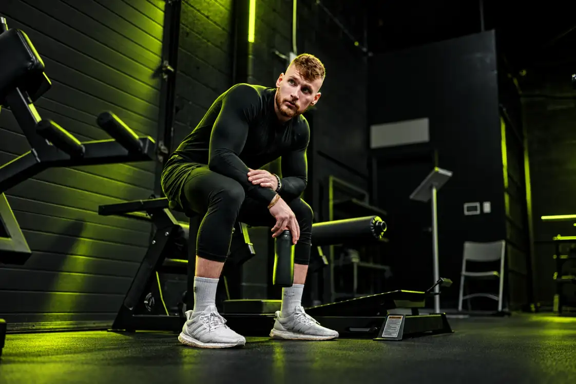 An athlete resting on a gym bench between sets, water bottle in hand